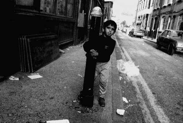 A boy secures himself around a bollard in Hanbury Street