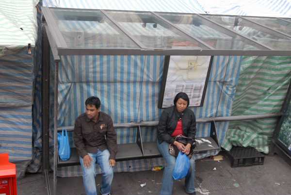 Two people wait for a bus in Whitechapel market, London 2009