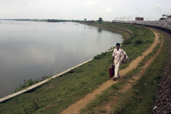 A man walks by a lake in the opposite direction to the train. Bangladesh 2008