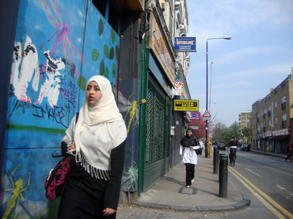 A woman walks past a blue entrance with graffiti. Vallance Rd, London 2009