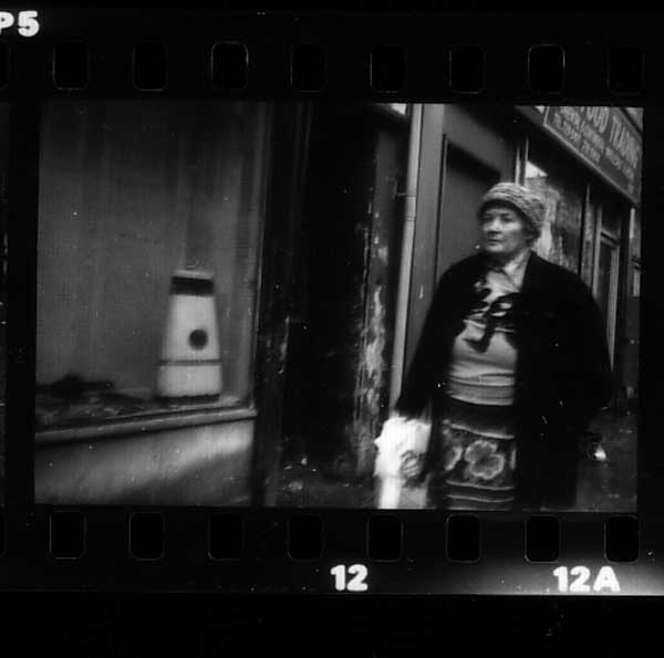 Lady passes shop window with oil heater. Brick Lane, London 1982