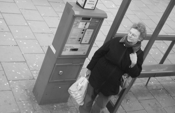 Woman at a bus stop. Mile End Road. East London March 2010.